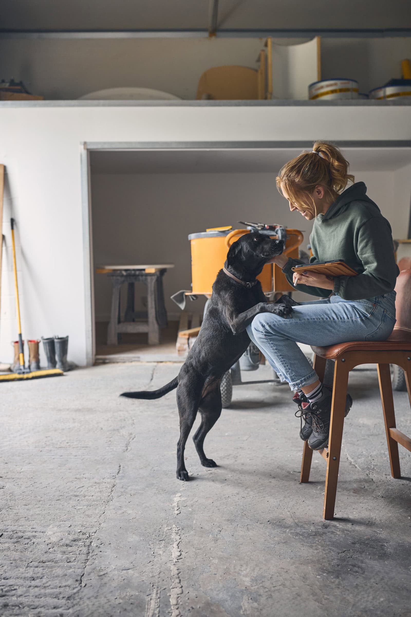 Female Worker Holding Digital Tablet With Pet Dog In Concrete Workshop